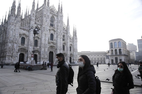 People wearing sanitary masks walk past the Duomo gothic cathedral in Milan, Italy, Sunday, Feb. 23, 2020. A dozen Italian towns saw daily life disrupted after the deaths of two people infected with t ...