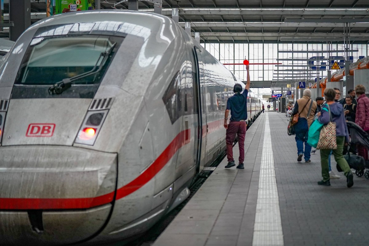 Deutschland, München, Bayern, Europa: ICE-Zug der Deutschen Bahn im Bahnhof, ein Bahnmitarbeiter gibt das Abfahrtssignal, wartende Reisende am Bahnsteig, moderne Mobilität, nachhaltiger Schienenverkeh ...