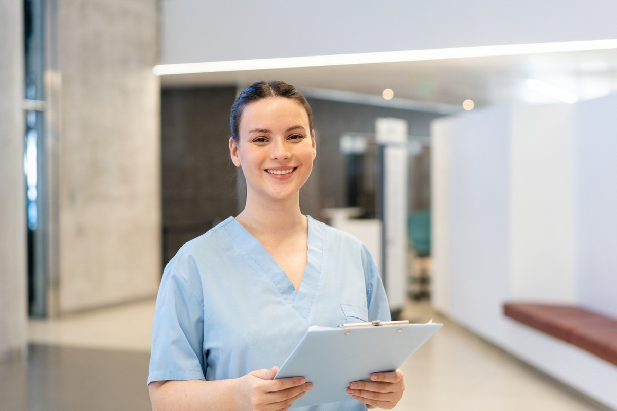 Portrait of happy female nurse with patient health report in hospital. Young woman standing in clinic holding a clipboard.