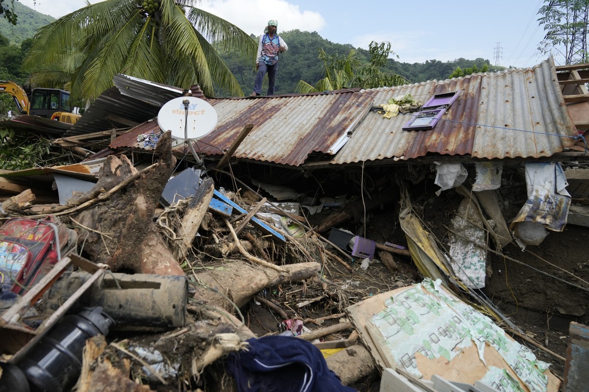 26.10.2024, Philippinen, Talisay: Marcelino Aringo steht auf einem beschädigten Haus, nachdem ein vom Tropensturm Trami ausgelöster Erdrutsch den Ort Talisay in der philippinischen Provinz Batangas he ...