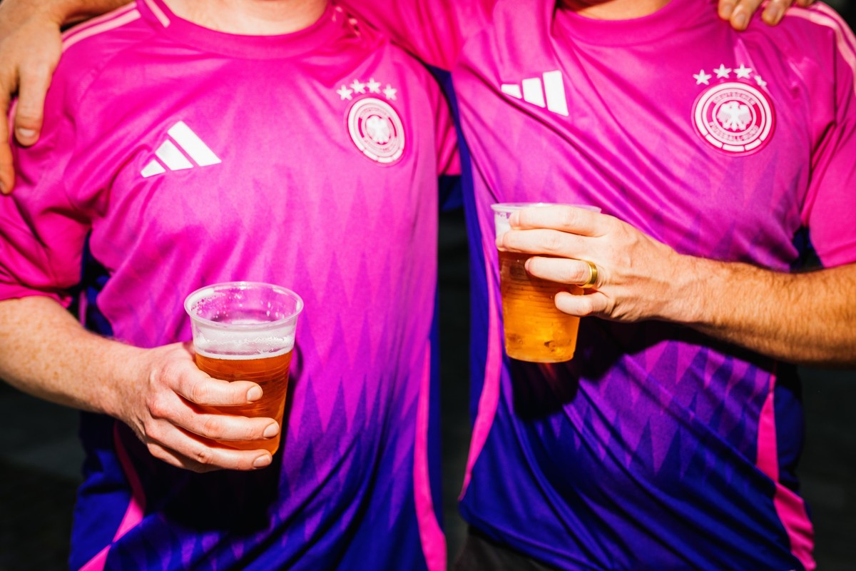 ARCHIV - 19.06.2024, Baden-Württemberg, Stuttgart: Fußball, EM, Public Viewing Deutschland - Ungarn. Zwei deutsche Fans tragen das Auswärtstrikot der deutschen Mannschaft und halten zwei Bierbecher in ...