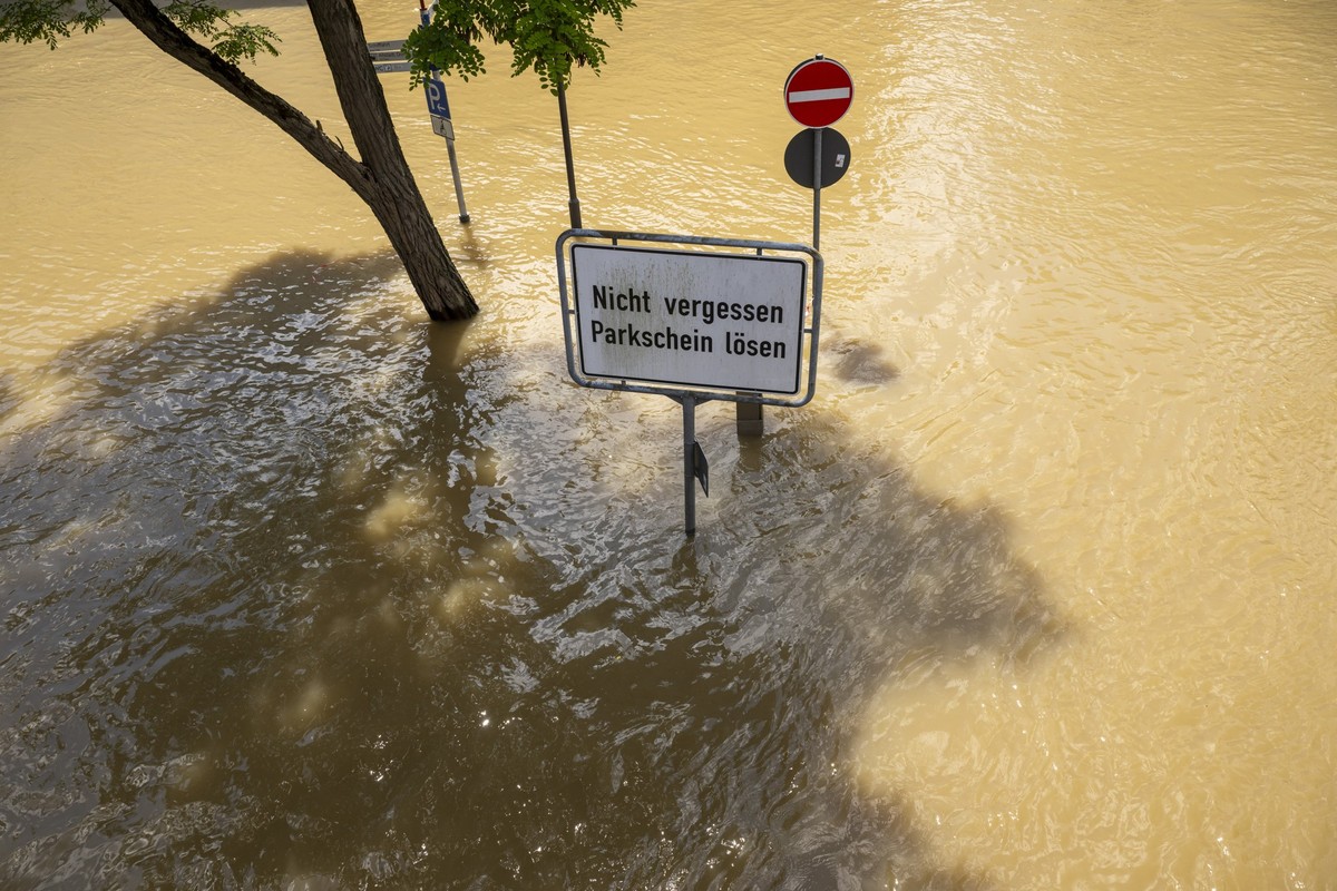 ARCHIV - 05.06.2024, Bayern, Passau: Ein Schild mit der Aufschrift &quot;Nicht vergessen Parkschein lösen&quot; steht auf einer überfluteten Strasse in der Dreiflüssestadt. In Bayern herrscht nach hef ...