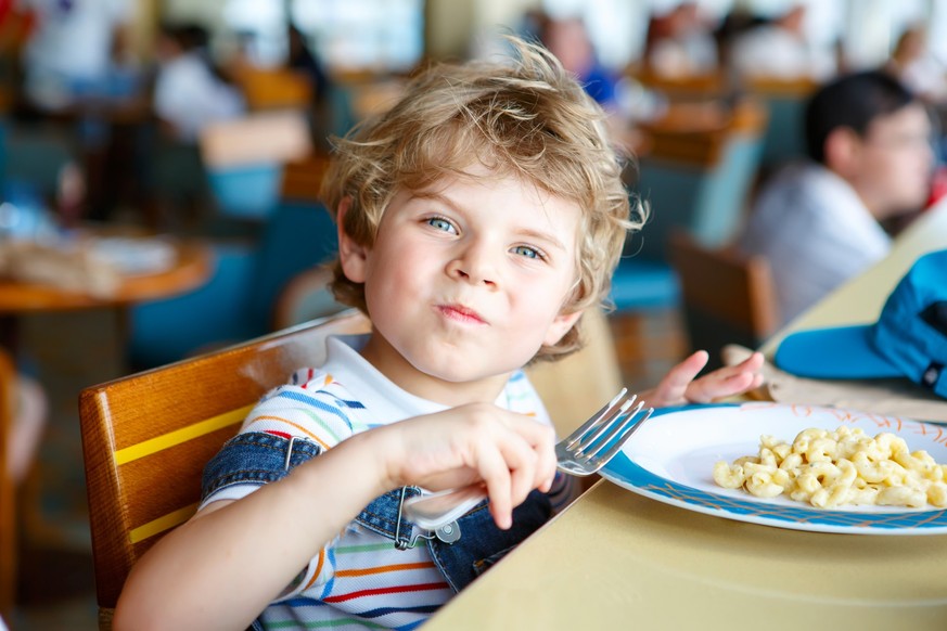Cute healthy preschool kid boy eats pasta noodles sitting in school or nursery cafe. Happy child eating healthy organic and vegan food in restaurant. Childhood, health concept