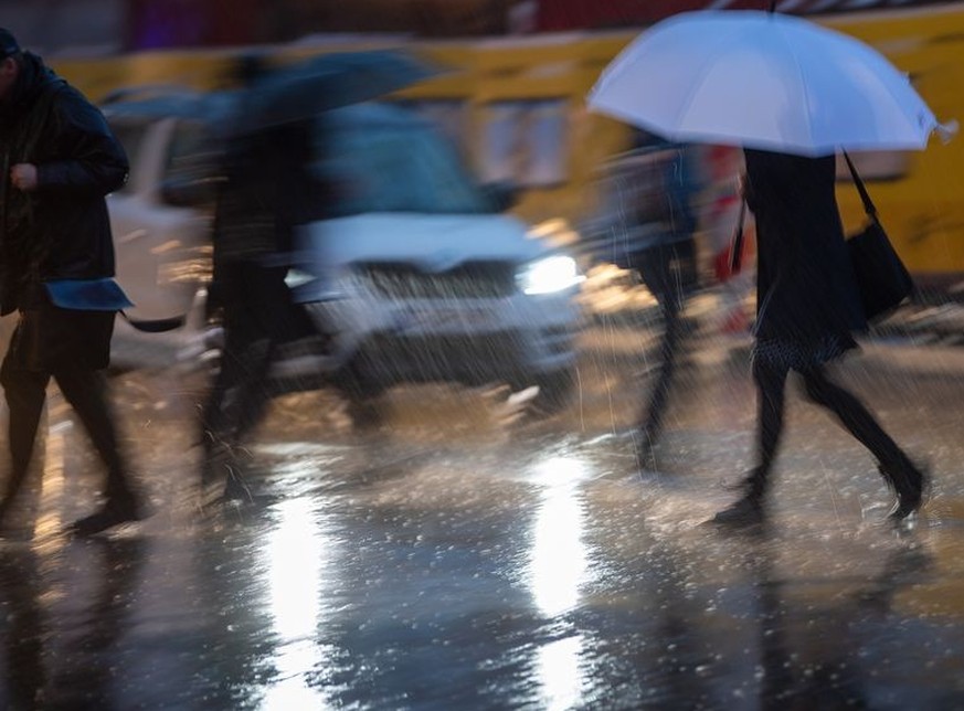 ARCHIV - 04.03.2019, Berlin: Passanten mit Regenschirmen gehen im Regen über die Straße. (zu dpa: «Wochenstart mit Sturm und Regen in Berlin und Brandenburg») Foto: Monika Skolimowska/dpa-Zentralbild/ ...