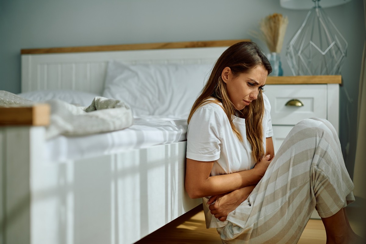 Young woman with stomach pain sitting on the floor in bedroom. Copy space.