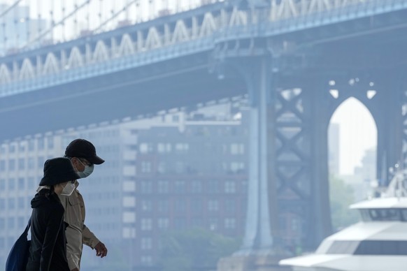 A couple wearing masks are framed by the hazy view of the Manhattan bridge while walking on the East River promenade, Thursday, June 8, 2023, in New York. Air pollution from Canadian wildfires are clo ...