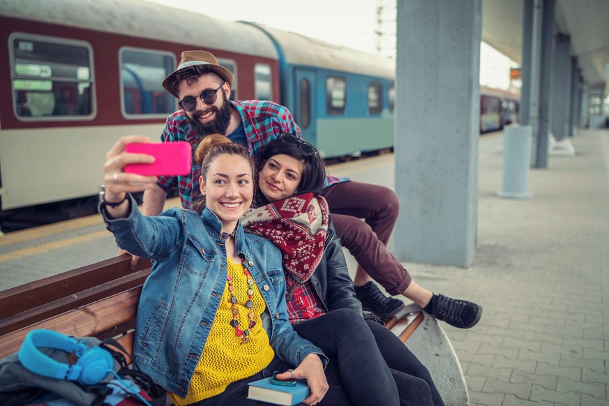 Cheerful young travelers waiting at the railway platform and making selfies