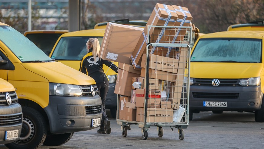 25.11.2022, Sachsen-Anhalt, Bitterfeld-Wolfen: Eine Mitarbeiterin der Deutsche Post DHL zieht einen vollen Paketwagen zu ihren Fahrzeug über den Hof eines Zustellpunktes. Die Wochen vor Weihnachten be ...