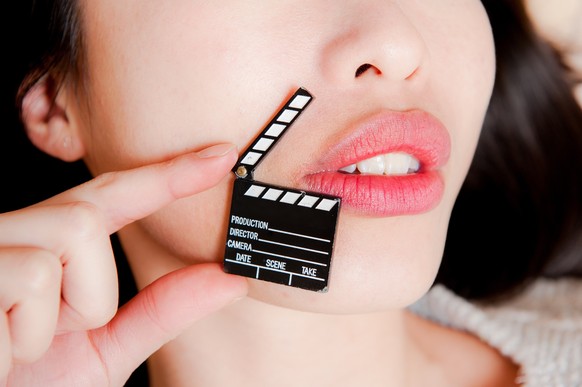 Face detail of sensual woman lips, no eyes, with hand holding little movie clapper board