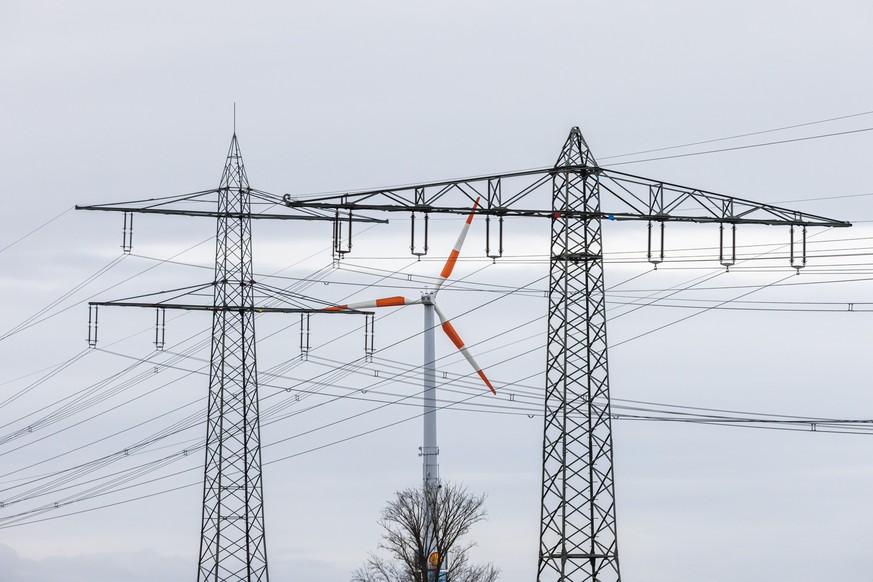 ARCHIV - 01.02.2022, Baden-Württemberg, Herbolzheim: Ein Windrad steht neben dem Mast einer Hochspannungsleitung und dreht sich im Wind. (zu dpa: «Kretschmann will schnelleren Ausbau der Stromtrassen» ...