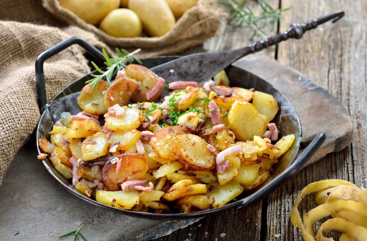 Hearty fried potatoes with onions and bacon served in an iron pan with rustic ambience