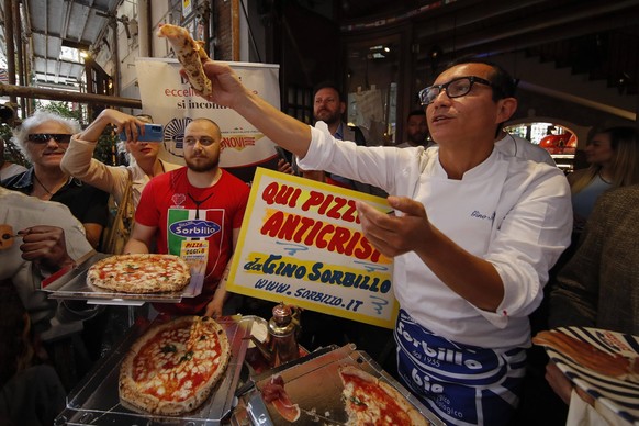 The well-known Neapolitan pizza maker Gino Sorbillo while explaining how to prepare a pizza, and also distributes slices to people and tourists who pass outside the historic location of the pizzeria i ...