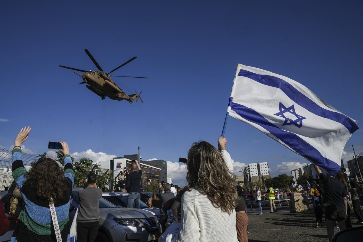 25.01.2025, Israel, Tel Aviv: Menschen mit israelischen Fahnen erwarten den israelischen Militärhubschrauber, der die vier aus dem Gazastreifen freigelassenen israelischen Soldatinnen an Bord hat und  ...