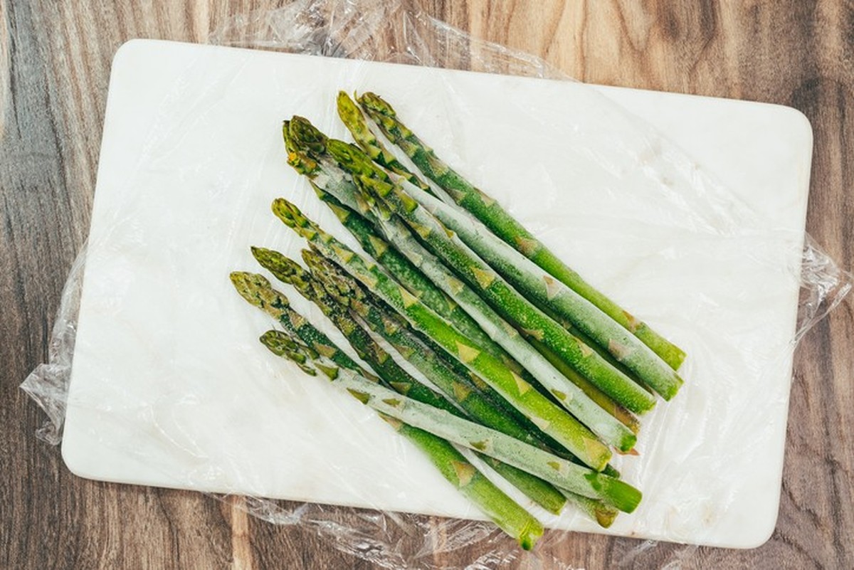 Frozen asparagus stalks close up on marble board on wooden background, directly from above