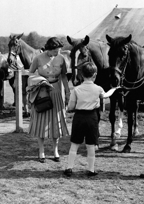 THE PRINCE OF WALES WATCHED BY THE QUEEN FEEDS ONE OF THE PONIES DURING A BREAK IN THE POLO TOURNAMENT, IN WHICH THE DUKE OF EDINBURGH WAS PLAYING AT SMITH'S LAWN IN WINDSOR GREAT PARK, BERKSHIRE.