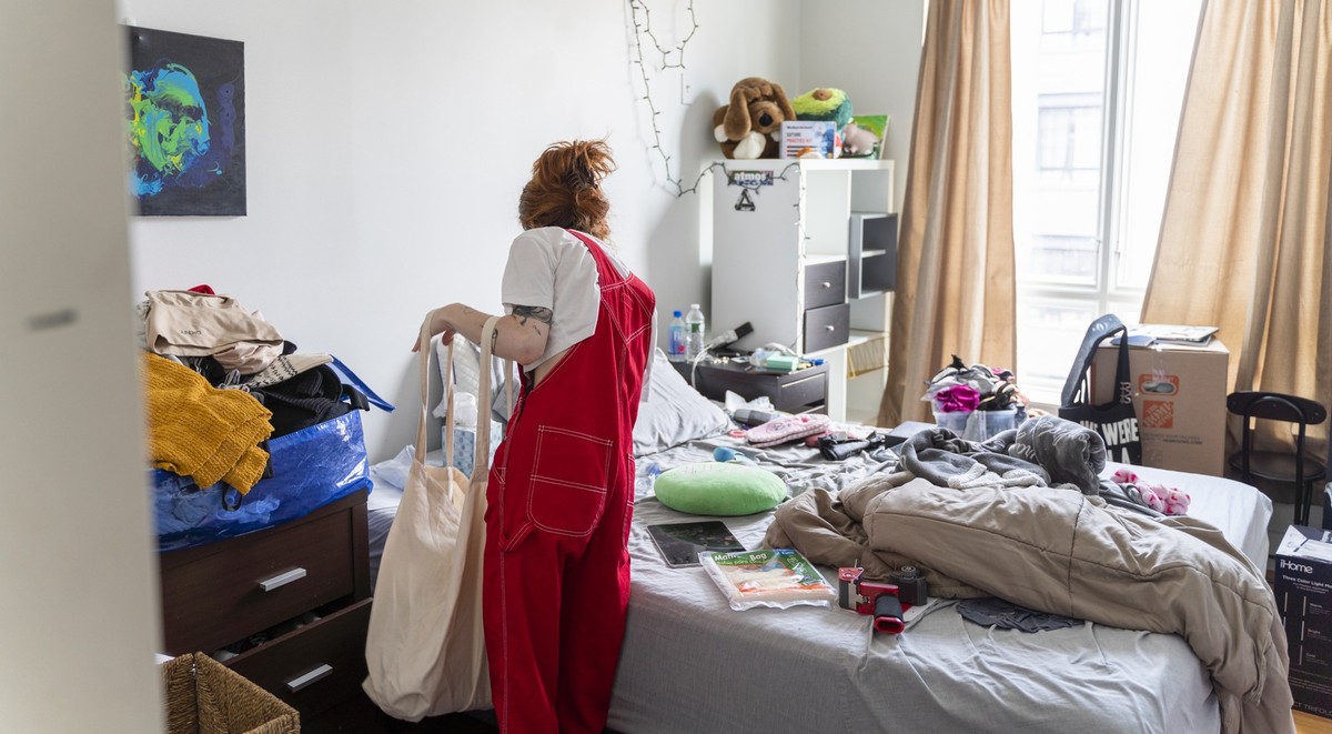 Young slender woman with brown long hair is packing her things to move. The room is a mess.