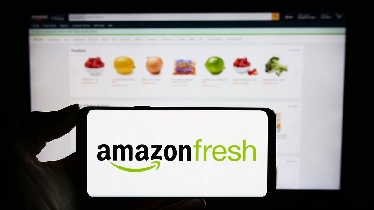 Person holding cellphone with logo of US grocery retail company Amazon Fresh in front of website. Stuttgart, Germany - 11-09-2023: Person holding cellphone with logo of US grocery retail company Amazo ...
