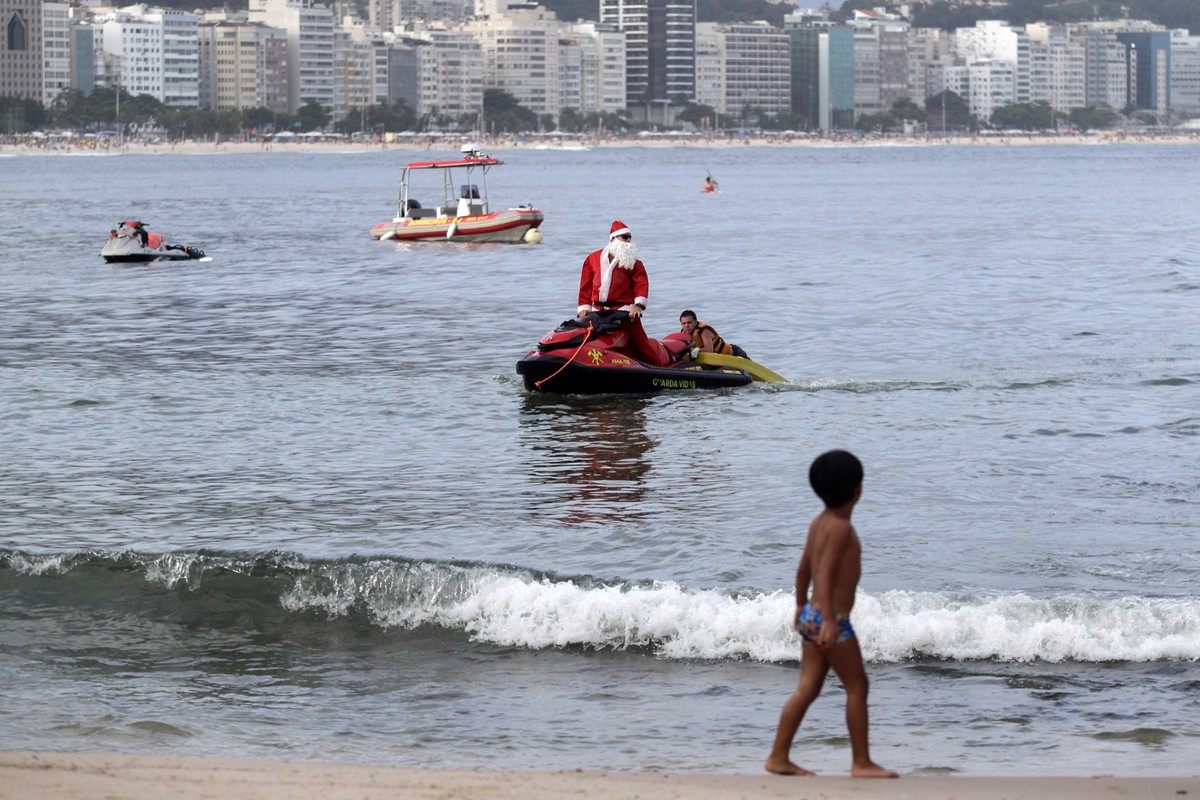 17.12.2024, Brasilien, Rio de Janeiro: Ein als Weihnachtsmann verkleideter Feuerwehrmann fährt mit einem Jetski am Strand der Copacabana in Rio de Janeiro. Foto: Bruna Prado/AP Photo/dpa +++ dpa-Bildf ...