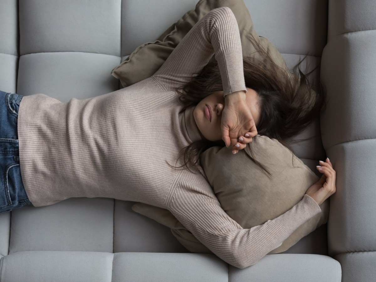 Peaceful pretty 20s girl lying on back on comfortable couch at home, covering eyes with hand, sleeping at daytime, feeling tired, enjoying relaxation, leisure, break, weekend. Top view xkwx person, wo ...