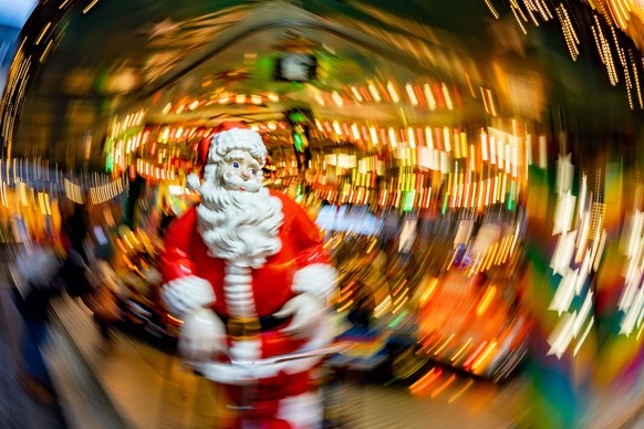 28.11.2022, Hessen, Frankfurt/Main: Eine lebensgroße Figur eines Weihnachtsmannes steht an einem Kinderkarrussel auf dem Frankfurter Weihnachtsmarkt (Aufnahme mit kreisförmig bewegter Kamera und länge ...