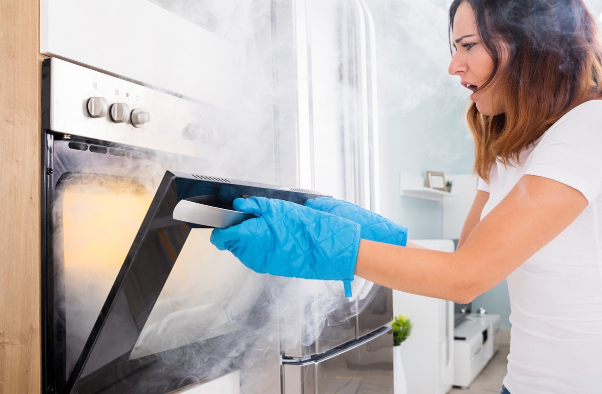 Young Unhappy Woman Opening Door Of Oven With Full Of Smoke