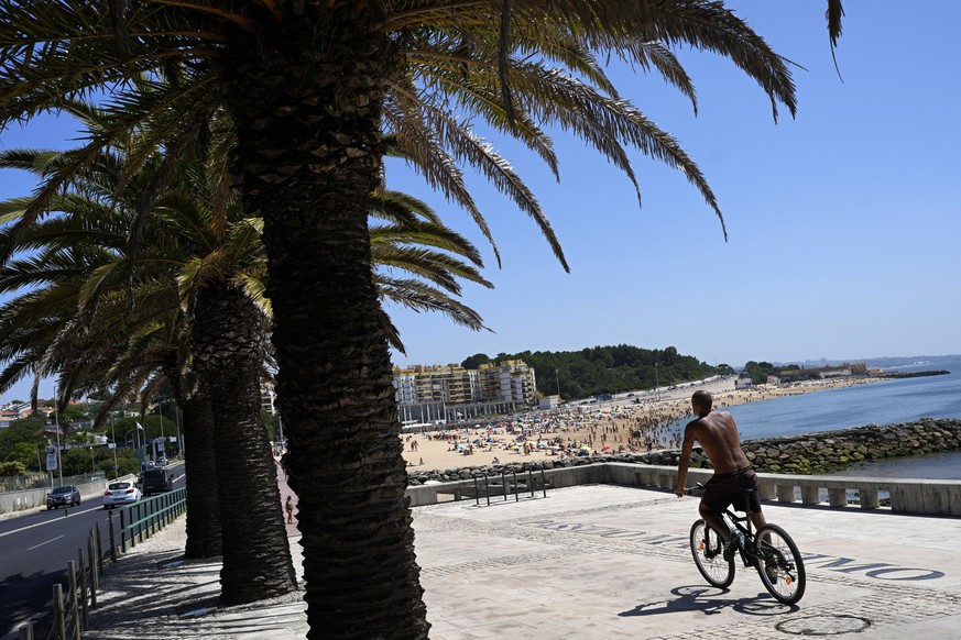 19.07.2023, Portugal, Oeiras: Ein Mann fährt mit dem Fahrrad am Strand von Oeiras. Portugal ist bisher von der Hitzewelle verschont geblieben, die weite Teile Südeuropas bei über 40 Grad Celsius hält. ...