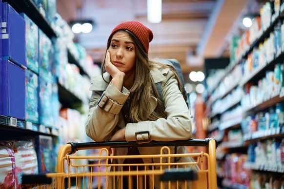 Young depressed woman with empty shopping cart in supermarket.