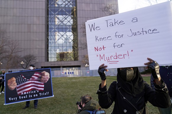 29.03.2021, USA, Minneapolis: Eine Demonstrantin h�lt w�hrend einer Pressekonferenz vor dem Gericht von Hennepin County ein Schild mit der Aufschrift �We take a knee for justice not for murder� (Wir k ...