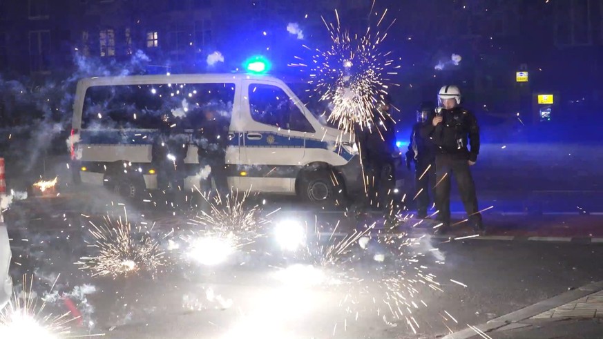 ARCHIV - 31.12.2022, Berlin: Polizeibeamte stehen am Silvesterabend hinter explodierendem Feuerwerk. (Zu dpa