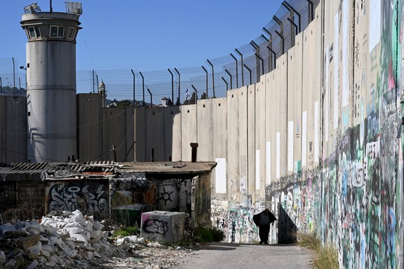 A Palestinian walks beside the the Israeli separation wall in the biblical town of Bethlehem, West Bank, on Monday, December 18, 2023. Bethlehem is normally packed with tourists but has been empty sin ...
