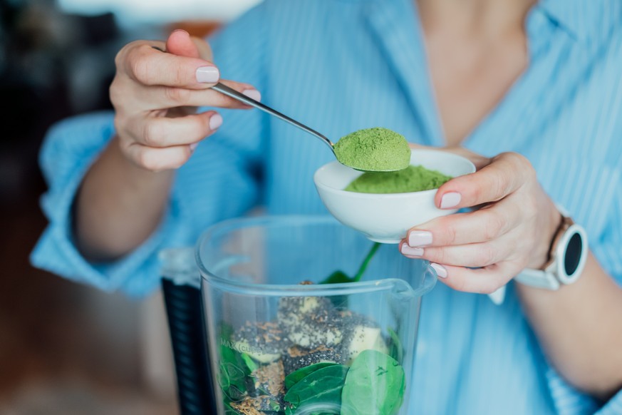 Close up woman adding wheat grass green powder during making smoothie on the kitchen. Superfood supplement. Healthy detox vegan diet. Healthy dieting eating, weight loss program. Selective focus.