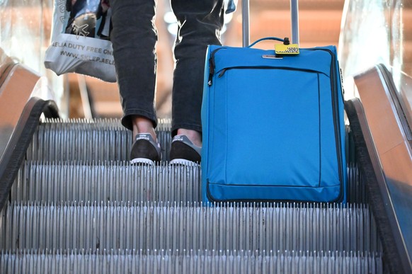 ARCHIV - 07.10.2022, Hamburg: Eine Frau f�hrt mit ihrem Koffer auf der Rolltreppe im Terminal 2. Mehr als jeder F�nfte in Deutschland kann es sich nicht leisten, eine Woche im Jahr in den Urlaub zu fa ...