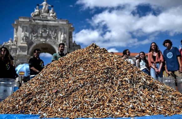 People look at a pile of cigarette butts, collected in one week, at Comercio square in Lisbon on April 23, 2023. - Environmental activists gathered in one week around 650,000 cigarette butts and piled ...