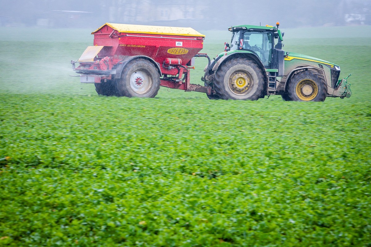PRODUKTION - 27.02.2024, Mecklenburg-Vorpommern, Dümmer: Ein Traktor fährt mit einem Streuwagen über ein Feld und bringt Dünger aus. Viele Landwirte in Norddeutschland blicken mit zunehmender Sorge au ...