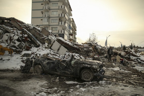 07.02.2023, Türkei, Malatya: Menschen sitzen vor einem eingestürzten Gebäude in Malatya. Rettungskräfte suchen weiterhin nach Überlebenden in den Trümmern tausender Gebäude, die durch ein starkes Erdb ...