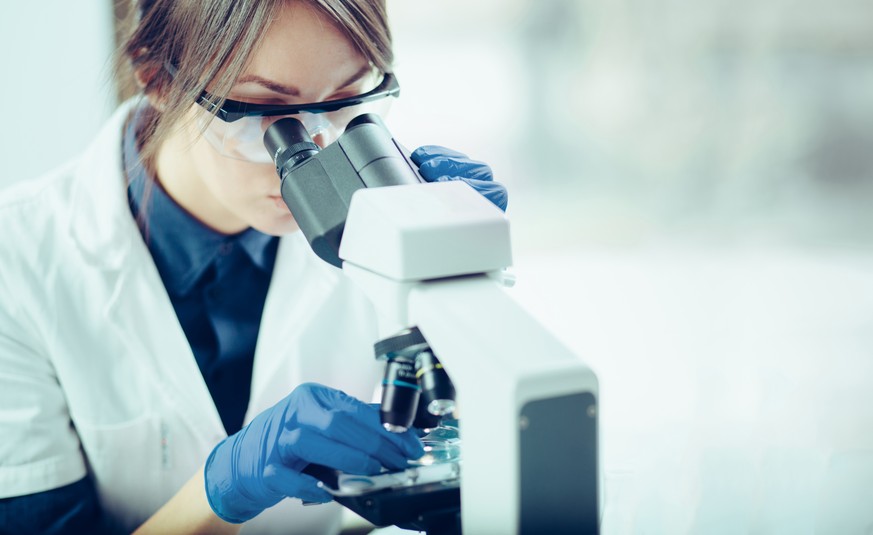 Young scientist looking through a microscope in a laboratory. Young scientist doing some research.