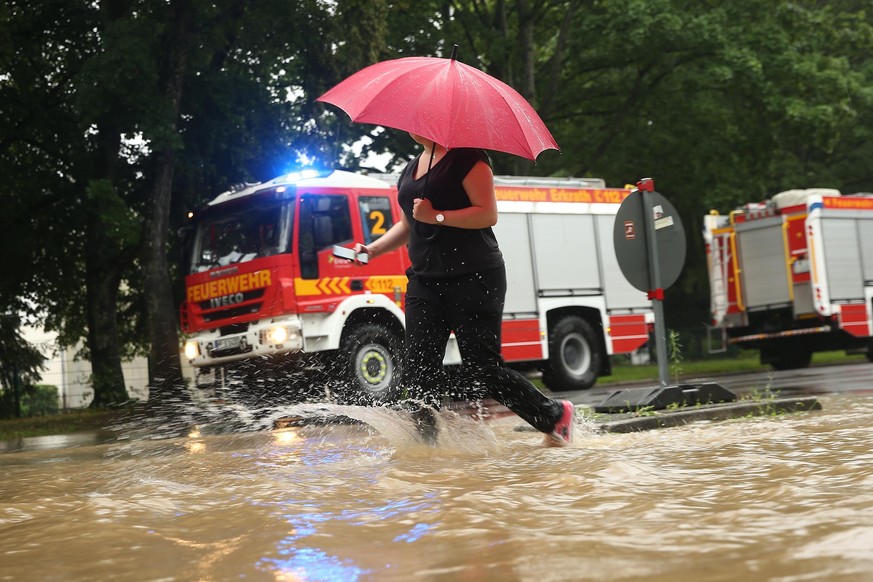 Eine Frau geht an Feuerwehrfahrzeugen vorbei mit einem Regenschirm über die Morper Allee.