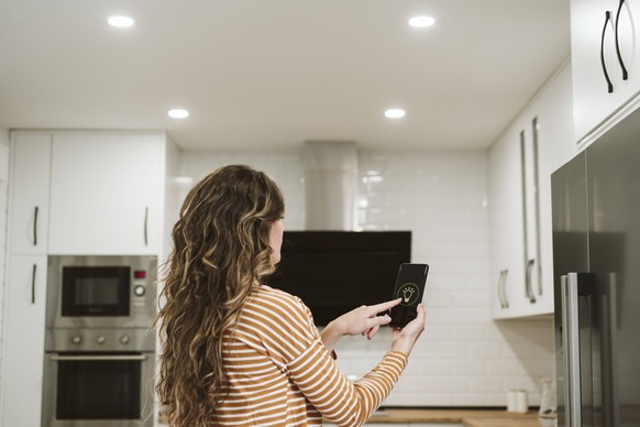 Young woman using mobile phone with smart home app for ceiling lights at home model released, Symbolfoto property released, EBBF06482