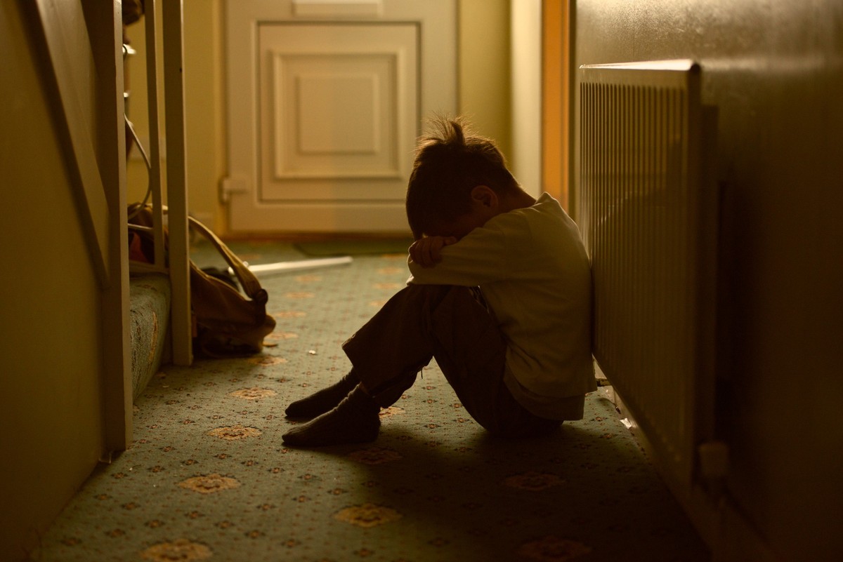 sad child with his head between his legs left alone at home