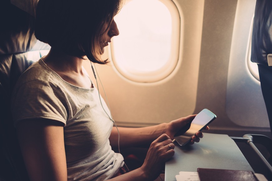 Young woman on a plane with a smartphone in her hands.