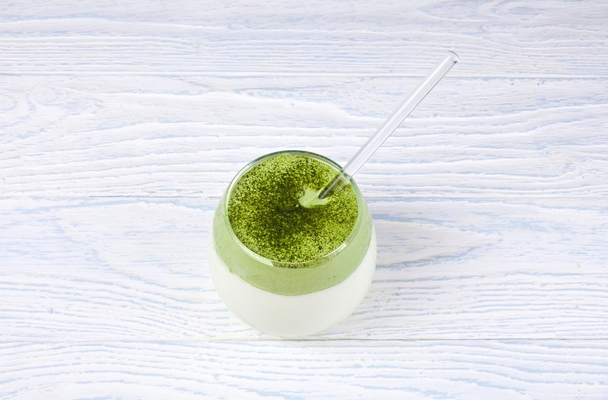 Dalgona matcha latte in a glass cup on a wooden background.