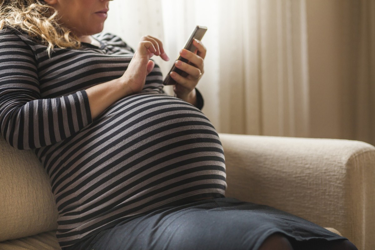 Beautiful pregnant woman with mobile phone in her bedroom