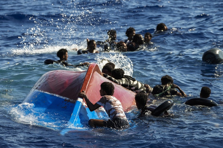 FILE - Migrants swim next to their overturned wooden boat during a rescue operation by Spanish NGO Open Arms at south of the Italian Lampedusa island at the Mediterranean sea, Aug. 11, 2022. Italy has ...