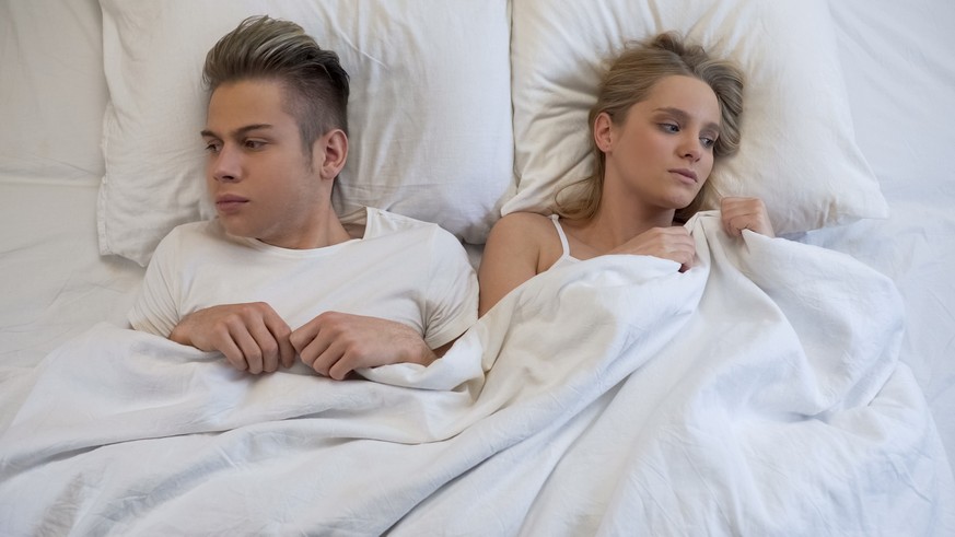 Upset young couple lying in bed, angrily pulling blanket, conflict in relations