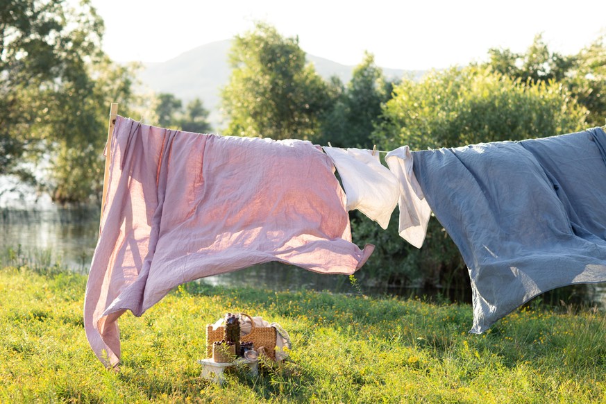 Pink and blue bedding sheet on forest background under the bright warm sun. Clean bed sheet hanging on clothesline at backyard. Hygiene sleeping ware concept.