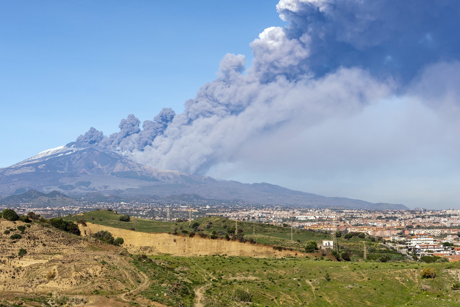 A smoke column comes out of the Etna volcano in Catania, Italy, Monday, Dec. 24, 2018. The Mount Etna observatory says lava and ash are spewing from a new fracture on the active Sicilian volcano amid  ...