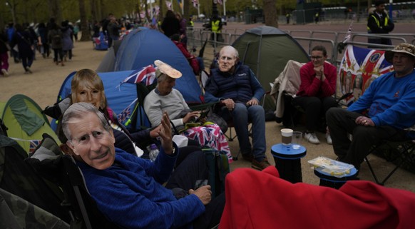 05.05.2023, Großbritannien, London: Schaulustige, die Masken von Mitgliedern der britischen Königsfamilie tragen, darunter König Charles III., campieren entlang der Mall, einem Teil der Krönungsroute. ...