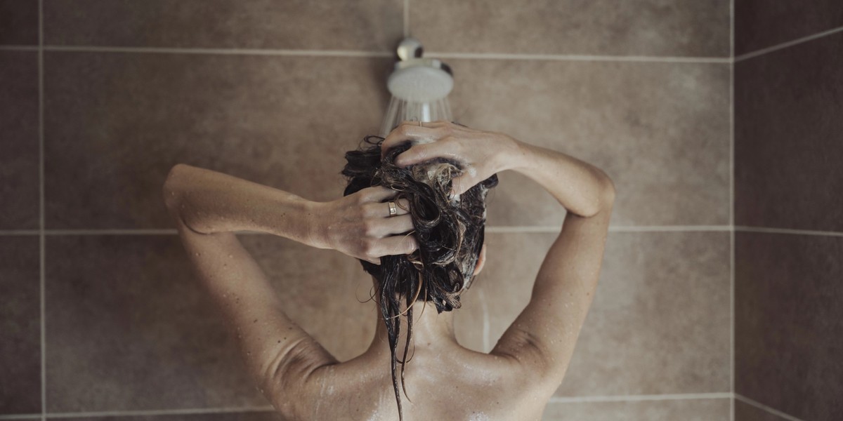View from behind of a woman showering and shampooing her hair in a domestic bathroom.