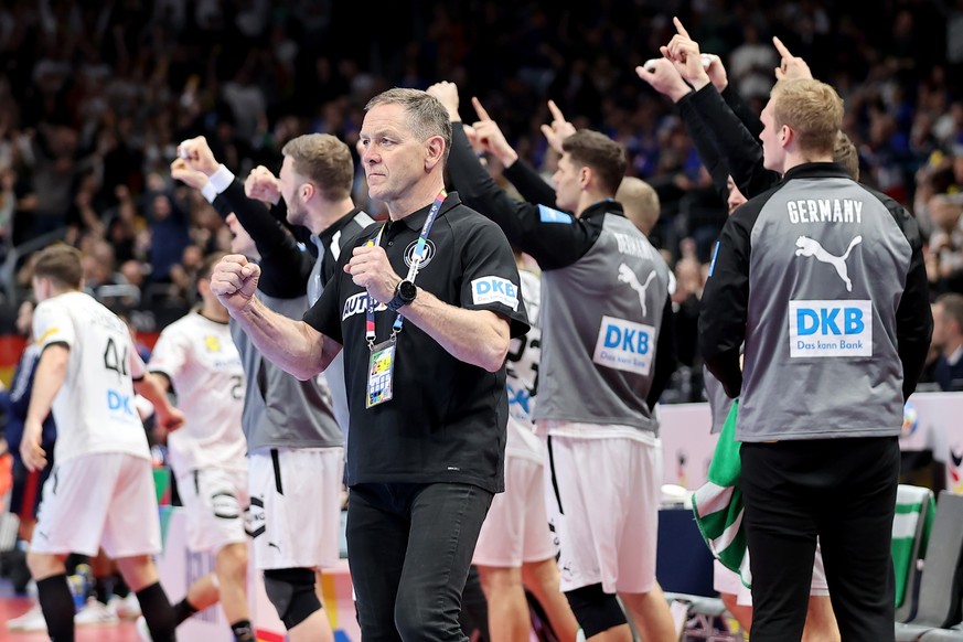 16.01.2024, Berlin: Handball: EM, Frankreich - Deutschland, Vorrunde, Gruppe A, 3. Spieltag, Mercedes-Benz Arena. Bundestrainer Alfred Gislason (vorn) und seine Spieler jubeln nach einer gelungenen Ak ...