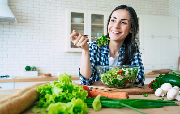 Healthy lifestyle. Good life. Organic food. Vegetables. Close up portrait of happy cute beautiful young woman while she try tasty vegan salad in the kitchen at home.